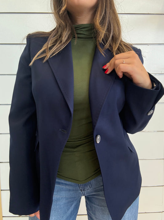 Giacca blu foderata con impunture indossata sopra una maglia verde e jeans, elegante per ogni occasione