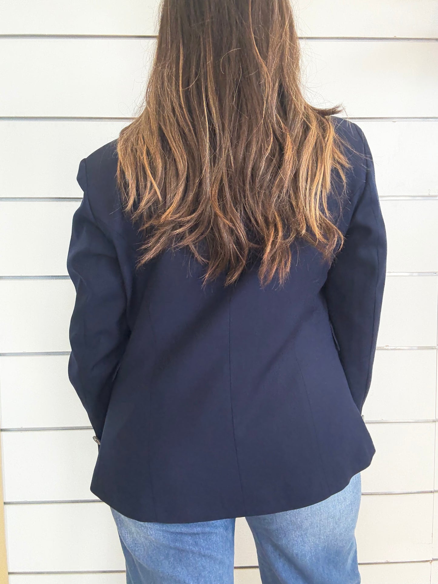 Giacca blu foderata con impunture vista da dietro su una modella con lunghi capelli castani
