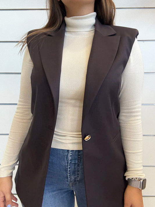 Gilet lungo da donna con bottone dorato in marrone, abbinato a maglione chiaro e jeans