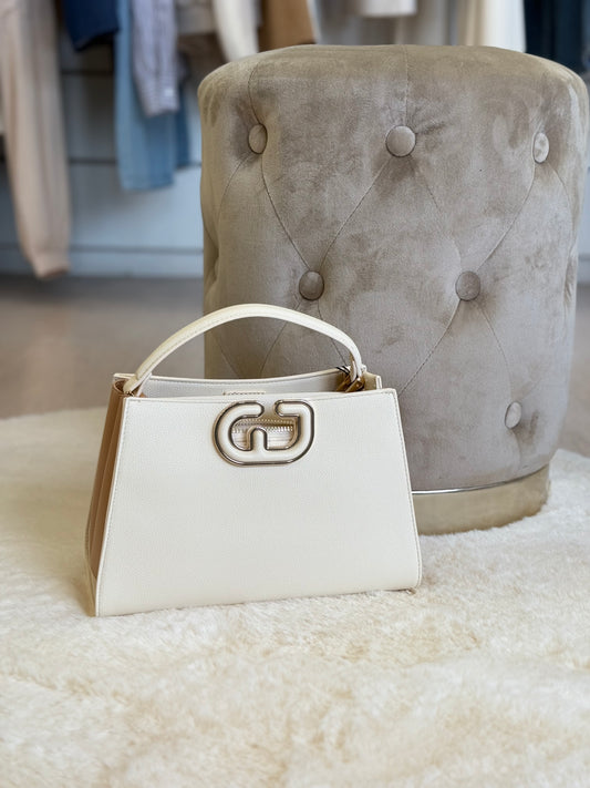 Borsa a mano e tracolla Gaudì in bianco e beige, elegante borsa classe e stile accanto a un pouf