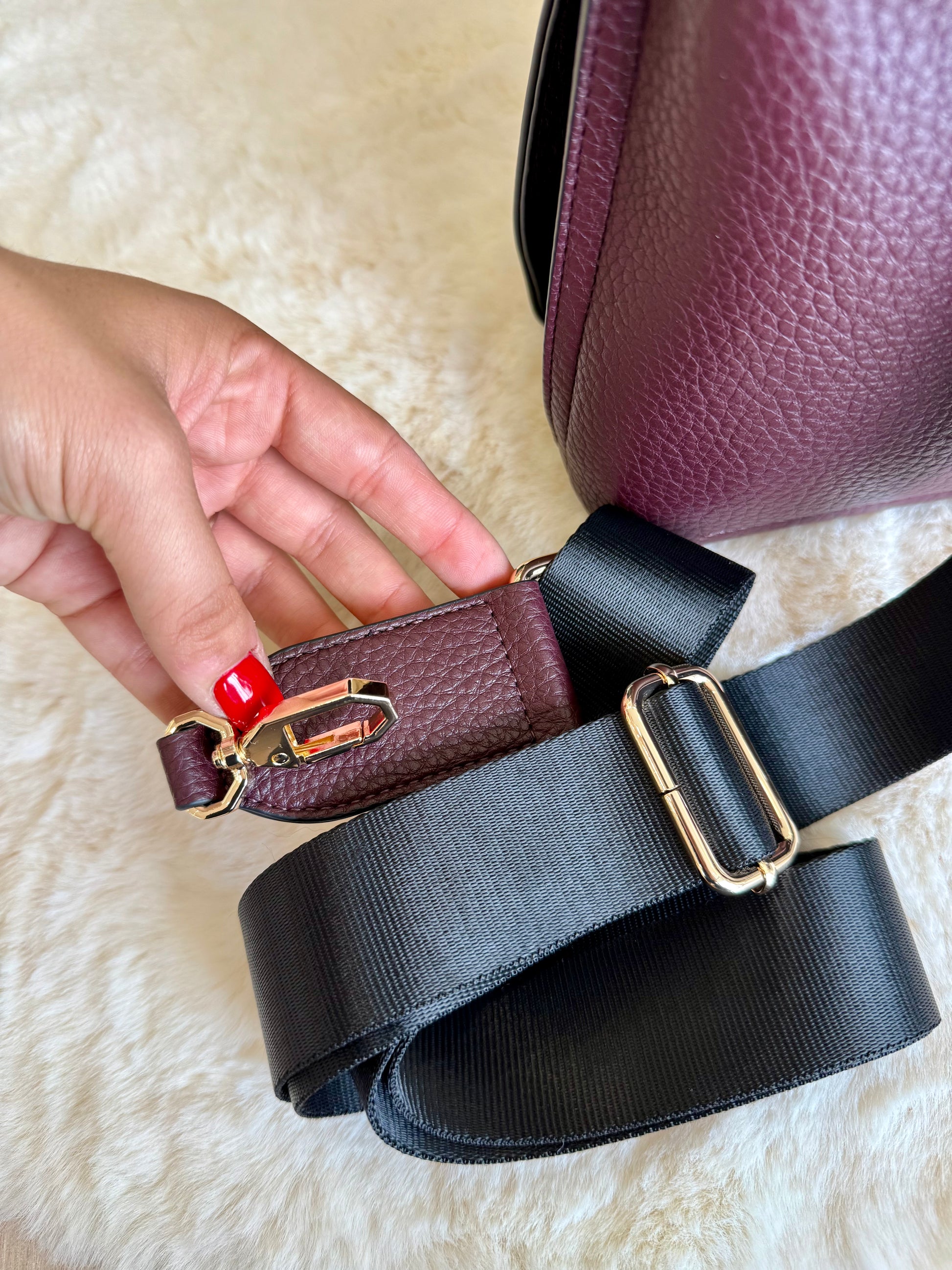Dettaglio della borsa top handle vinaccia in similpelle con una mano che tiene il manico