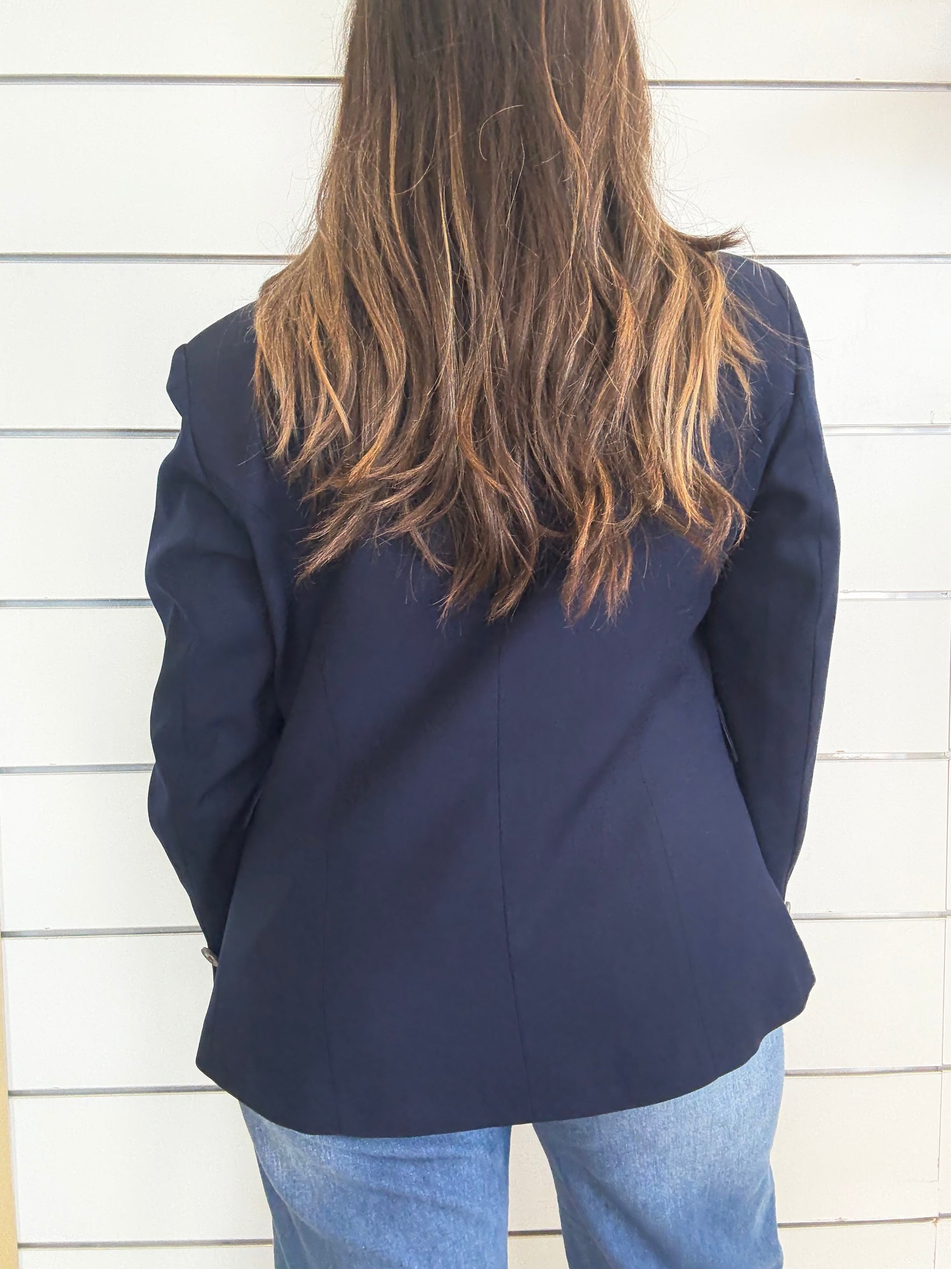 Giacca blu foderata con impunture vista da dietro su una modella con lunghi capelli castani