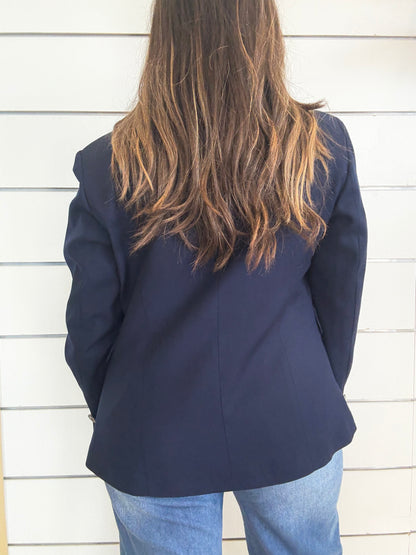 Giacca blu foderata con impunture vista da dietro su una modella con lunghi capelli castani