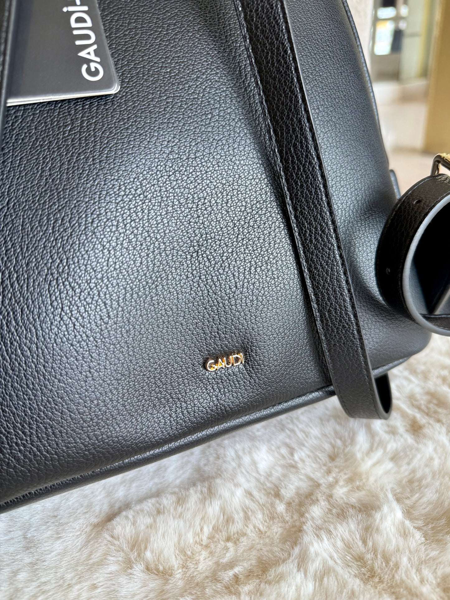 Dettaglio dello zaino nero in similpelle Gaudì con logo dorato su fondo in ecopelle